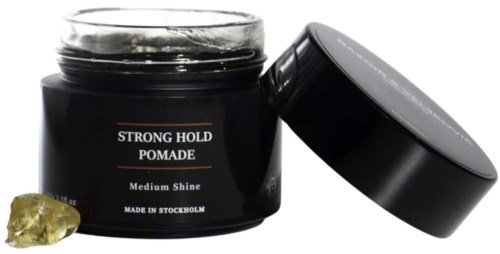 A black jar of holding pomade labeled 'Strong Hold' with its lid off and a small shiny gold stone nearby.