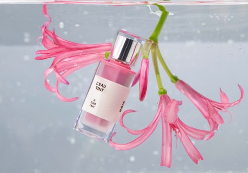 Pink flowers are floating in water with a pink perfume bottle. The bottle is tilted and partially submerged.