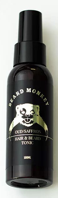 Sort flaske med skæg- og hårtonic med en abe-logo og hvid tekst. Fokuser på produktets label.