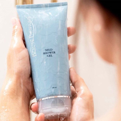 En person håller ett blått rör med duschgel märkt 'Mild Shower Gel'. Vatten syns på händerna.