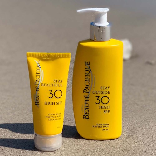 Två gula solkrämflaskor med SPF 30, en för ansiktet och en för kroppen, placerade på sandig yta.