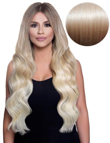 En kvinde med langt, blond, bølget hår, iført sort top, smilende, med en cirkulær hårfarveprøve over.