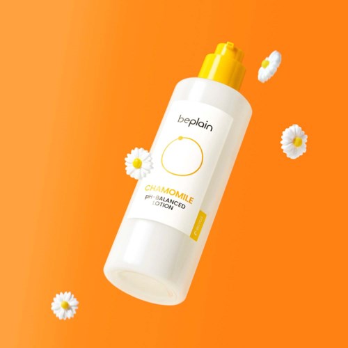 Een witte fles met 'Kamille' erop en een gele dop, omgeven door kamillebloemen op een oranje achtergrond.