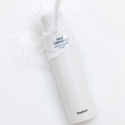 Eine weiße zylindrische Flasche mit dem Etikett 'Milk Ceramic Moisturizing Toner' wird mit Wasser übergossen.