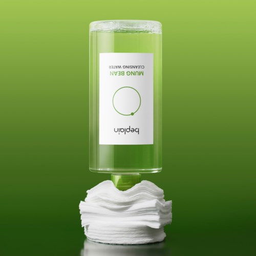 En genomskinlig grön flaska märkt 'Mungo Green' upp och ner med en prydlig stapel bomullspads under.
