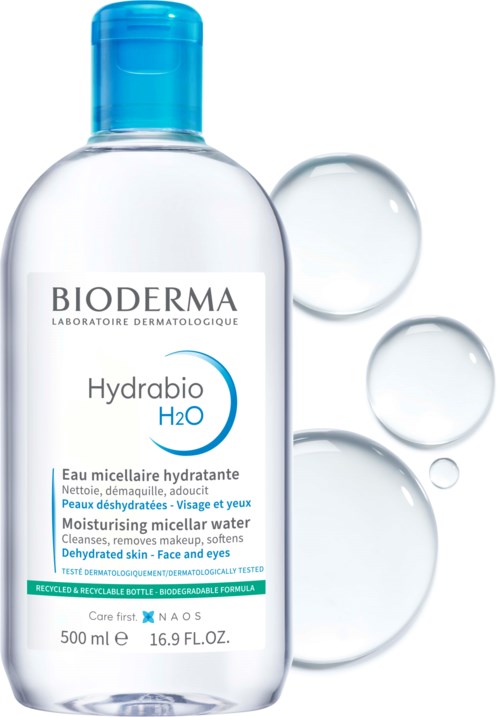 En klar flaske med blå lokk som inneholder Hydrabio micellar vann, omringet av vanndråper.