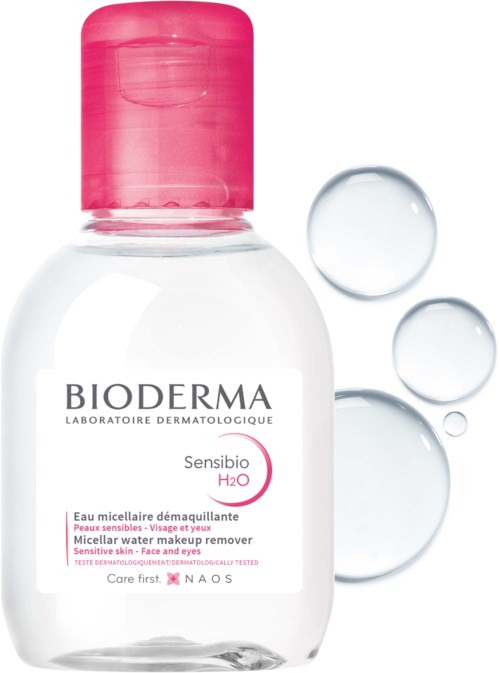 En liten vit flaska med rosa lock, märkt Bioderma Sensibio H2O, med tre vattenstänk i närheten.