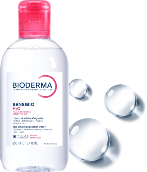 En flaska Bioderma Sensibio H2O micellarvatten, med tre droppar bredvid, märkt för känslig hud.
