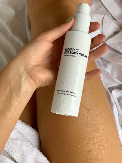 En person håller en vit flaska märkt 'Bioeffect EGF Body Serum' med vattendroppar på huden.