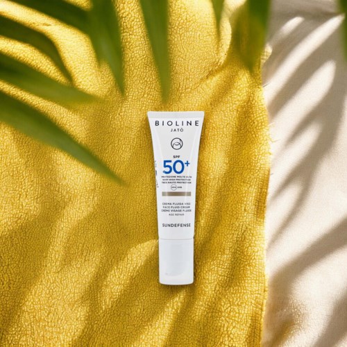 En solskyddsgrädde med SPF 50+ på en gul handduk med skuggor.