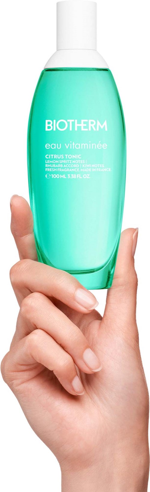 En hånd holder en grønn flaske med Biotherm Eau Vitaminée Citrus Toner.