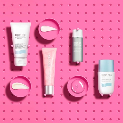 Hudplejeprodukter med pink baggrund, inklusive cremer, en tandbørste og små skåle til påføring.