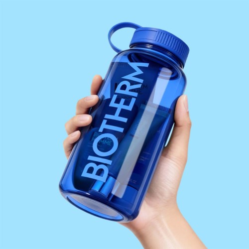 En hand håller i en blå behållare märkt BIOTHERM mot en ljusblå bakgrund.
