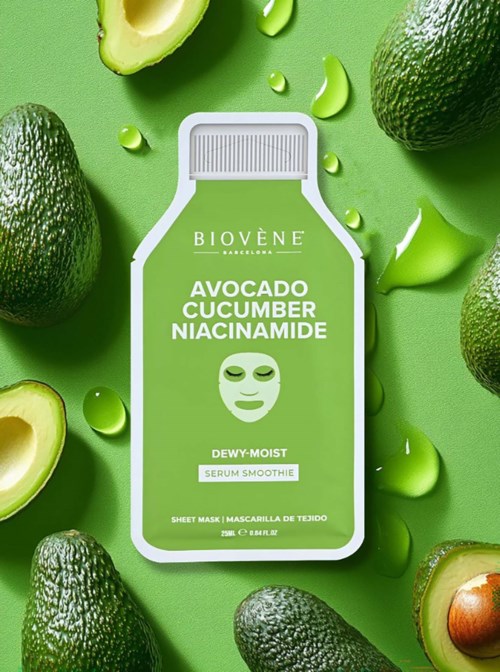 En ansigtsmaskeindpakning omgivet af avocado, agurkestykker og grønne serumdråber på en grøn baggrund.