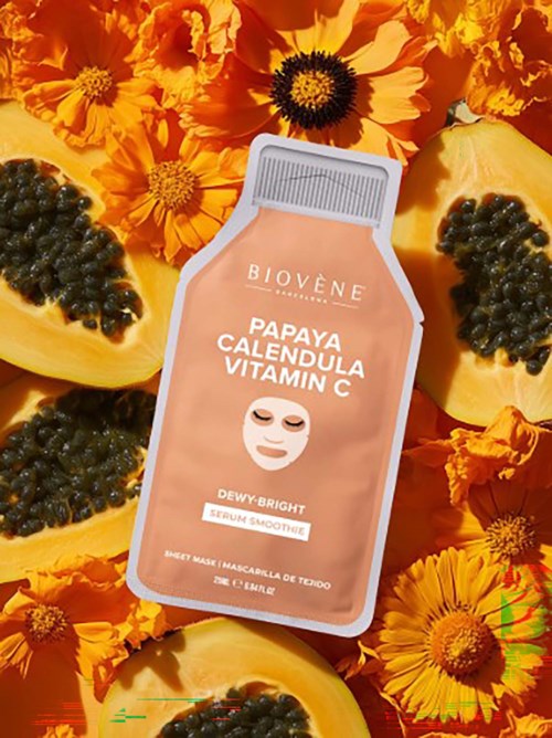 Kasvonaamio, jossa on papaijaa, kalendulaa ja C-vitamiinia, on asetettu osaksi papaijaleikettä ja kirkkaan oransseja kukkia.