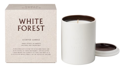 Ett vitt ljus i en vit hållare bredvid sin förpackning märkt 'White Forest', med brunt lock och en liten matchande skål.
