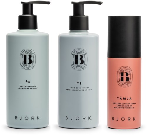 Tre flaskor med hårvårdsprodukter, två med pump och en spray, med enkla etiketter och pastellfärger.