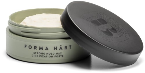 A round, black lid open to show white wax inside, with a light green container label and text.