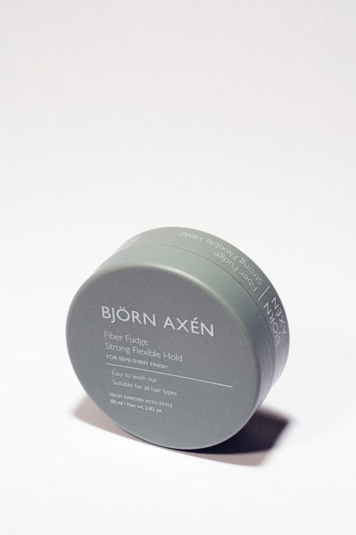 Een grijze ronde container met zwarte tekst, labelt Björn Axén Fiber Fudge voor haarstyling.