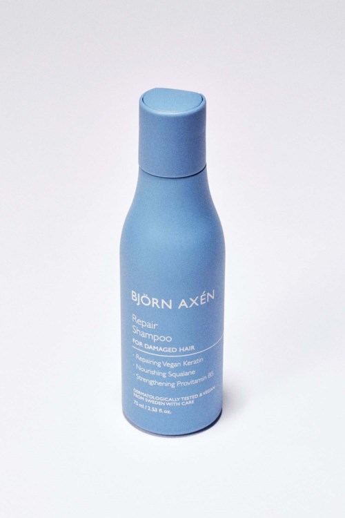 Niebieska butelka z napisem 'Björn Axén Repair Shampoo' dla zniszczonych włosów.
