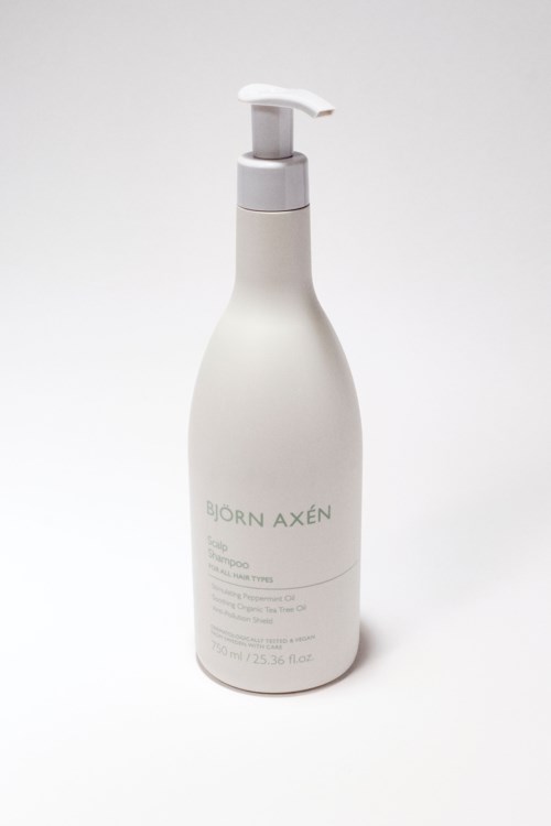 Biała butelka z pompką, oznaczona jako produkt do włosów Björn Axén, na prostym tle.