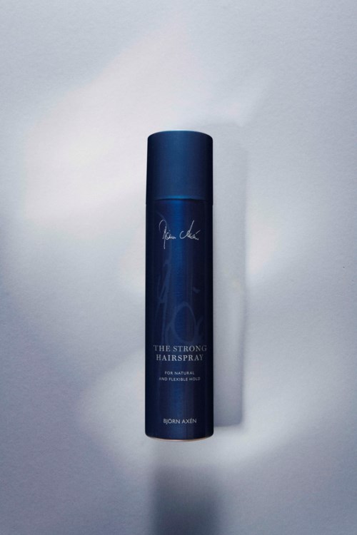 En blå hårsprayflaska med namnet 'The Strong Hairspray' av Bjorn Axen med enkel design på ljus bakgrund.
