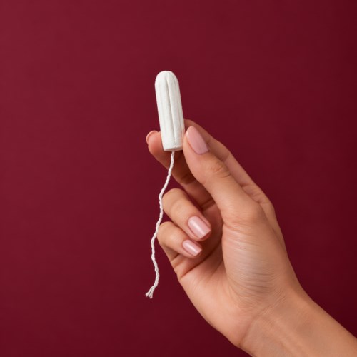 En hand håller en vit menstruationskopp mot en röd bakgrund.