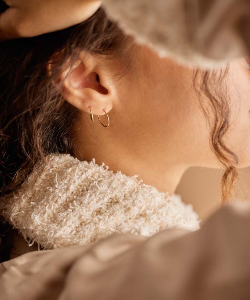 Close-up of a woman's neck, ear with hoop earring, and soft scarf, with wavy hair and warm lighting.