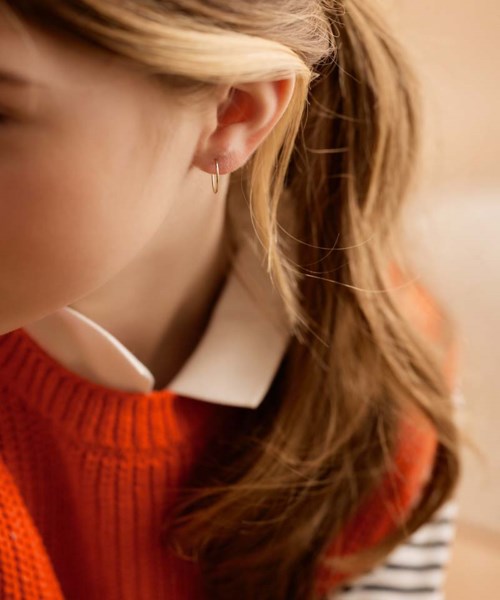 The image shows a close-up of a woman with blond hair wearing an orange sweater and a white shirt, focusing on her ear and hair.