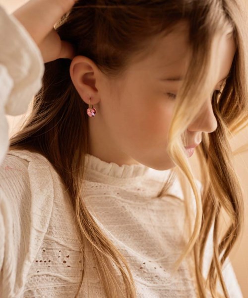Een jonge vrouw met lang haar glimlacht, draagt oorbellen en een wit, gemerkt topje, raakt voorzichtig haar haar aan.