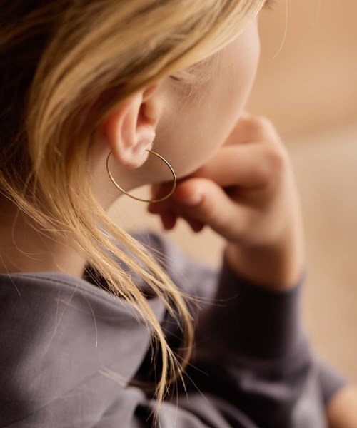 A person with long hair, wearing a hoop earring, touches their face, sitting in a warm environment.
