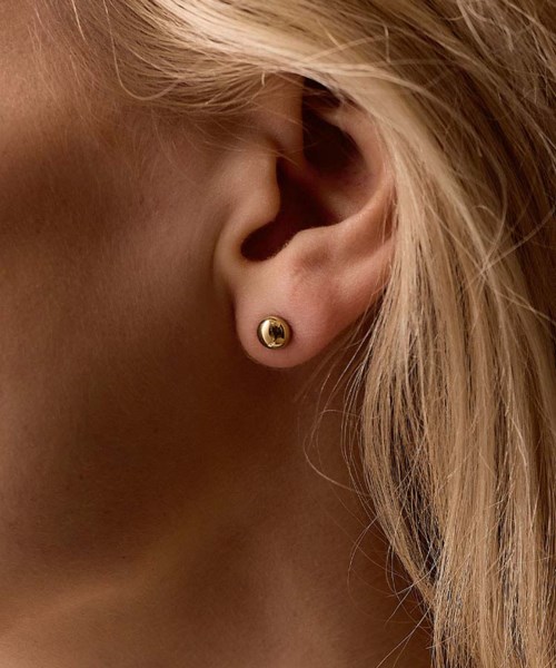 Close-up of a woman's ear with a gold stud earring, blonde hair, and part of her face visible.