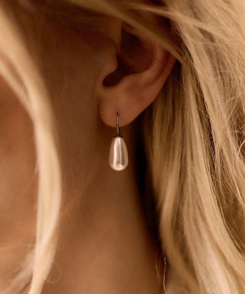 En kvinna har en silverdroppeörhänge på sitt öra med blond hår som delvis täcker hennes ansikte.