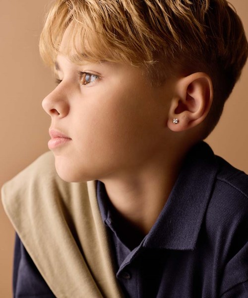 A young boy with blonde hair and blue eyes looks to the left, wearing a dark shirt and light-colored jacket.