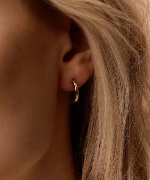 Close-up of a woman's ear with a small gold hoop earring and blonde hair.