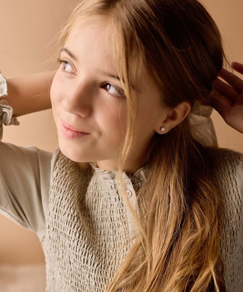 En ung jente med blondt hår og et mildt smil, ser oppover med hånden bak hodet.