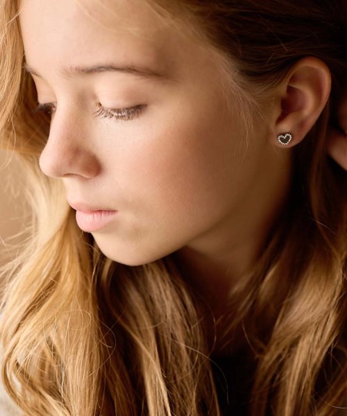 A woman with closed eyes, long blonde hair, and a small heart-shaped earring.
