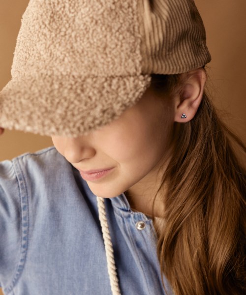 A girl with long hair wearing a beige cap and blue shirt, smiling slightly and looking down.