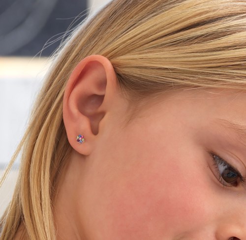 Close-up of a young girl's ear with colorful flower-shaped earrings.