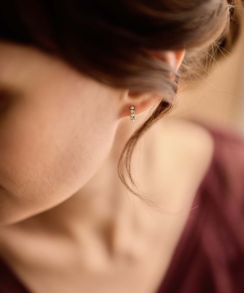 Close-up of a woman's ear with small gold hoop earrings, part of her face and brown hair visible.