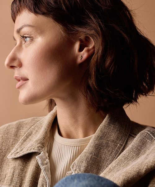 Side profile of a woman with short brown hair wearing a beige jacket and a white top.