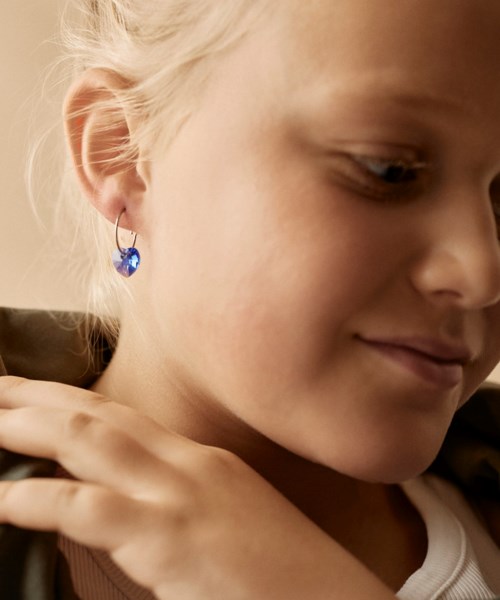 Nuori tyttö, jolla on vaaleat hiukset ja sininen korvakoru, hymyilee varovasti ja pitää kättä olkapäällä.