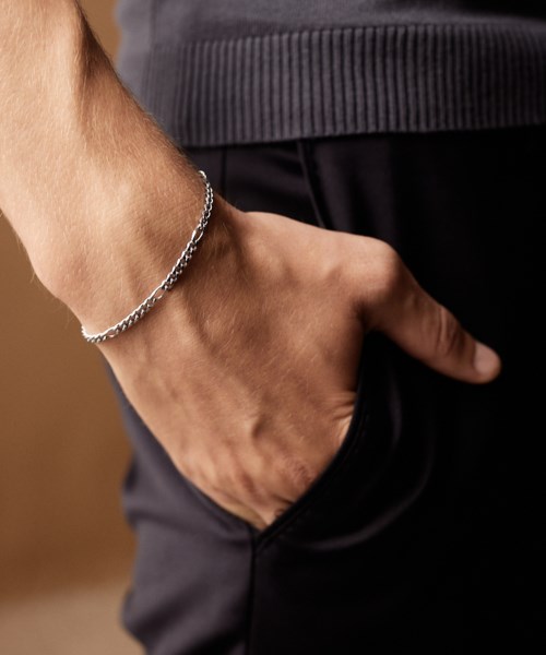 A person wearing a silver bracelet with their hand in their pocket, dressed casually with a striped gray top.