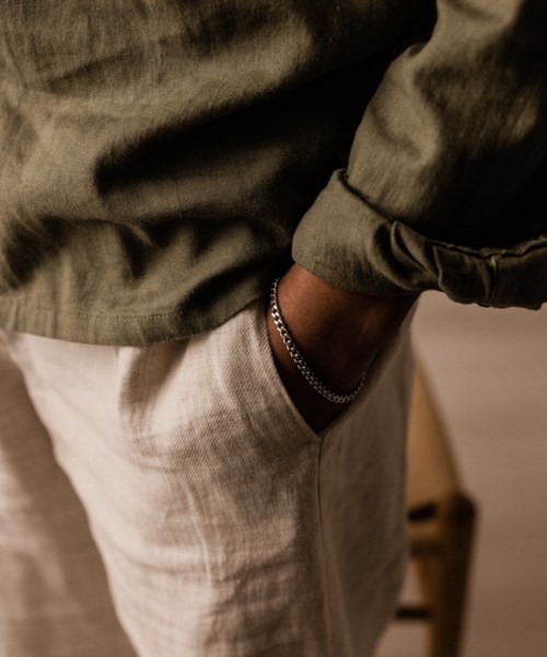 Eine Person trägt eine grüne Jacke und beige Hosen mit einer Hand in der Tasche.