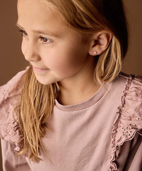 Side view of a smiling young girl with long blonde hair, wearing a pink top with ruffled sleeves.