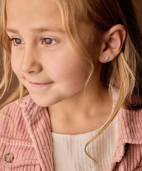 A young girl with blonde hair, wearing a pink jacket and earrings, looking to the side.