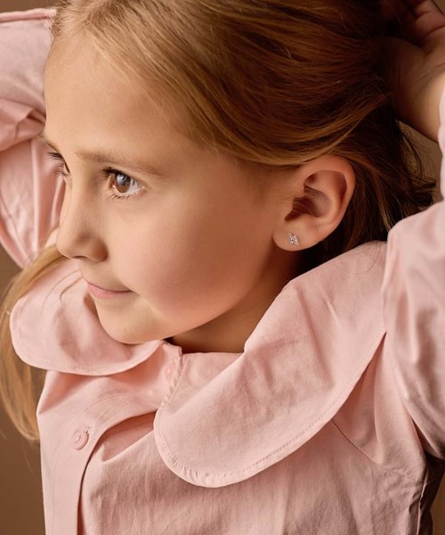 A young girl with red hair wearing a pink jacket, looking to the side with a gentle smile.