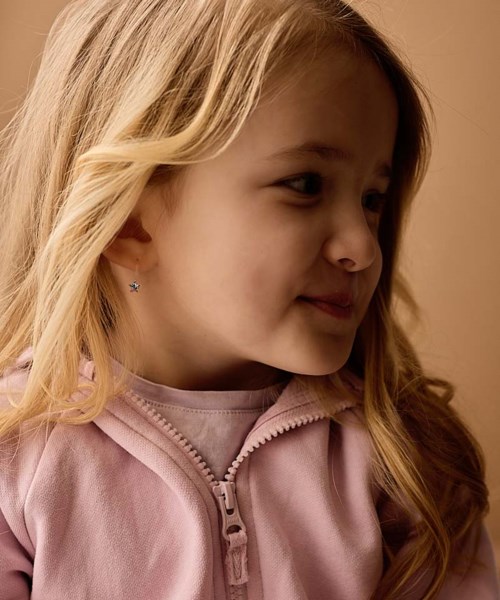 A girl with long blonde hair wearing a pink zip-up hoodie, looking to her right with a gentle smile.