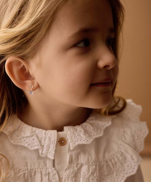 Profile of a young girl with earrings and a white top with lace details, looking to the side.
