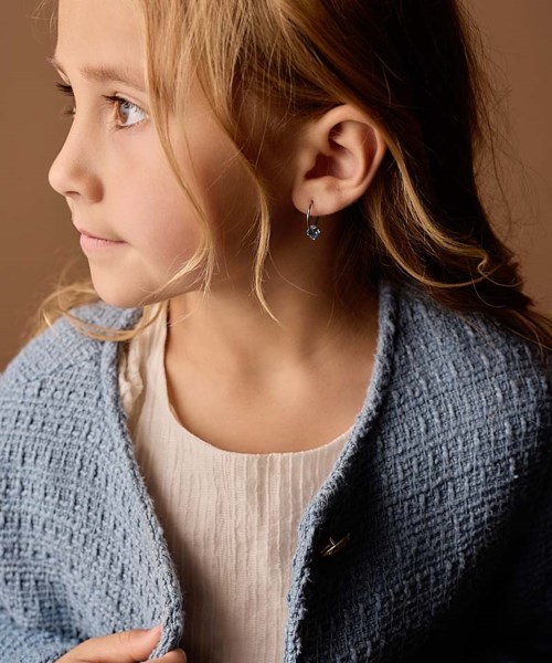 Ung pige med blond hår, iført en lys grå strikket cardigan og en hvid top, ser til venstre.